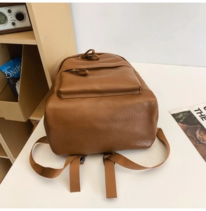 Close-up of brown PU leather backpack bottom showing stitching and strap attachment