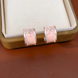 Macro view of pink enamel bow hoop earrings resting on a brown jewelry display box
