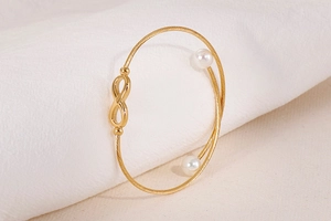 Detail van gouden infinity armband met gedraaide textuur en witte schelpparels