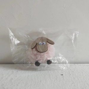 Close-up of a pink felt sheep ornament with wooden limbs in transparent packaging