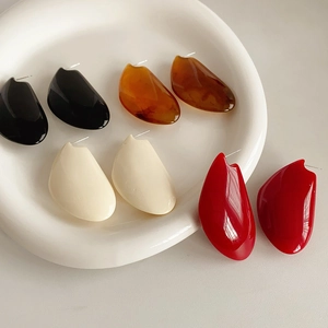 Vue à plat de boucles d'oreilles en résine ambre, noir, crème et rouge sur une assiette blanche