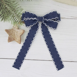 Detail of a navy denim bow hairclip with white wavy ric-rac edges on a wooden background