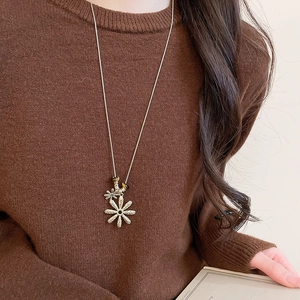 Detailed close-up of golden daisy pendant necklace styled on a brown knitted sweater