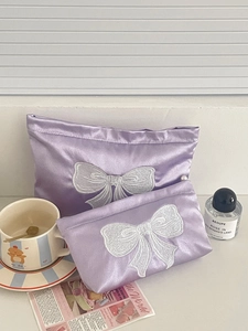 Detail of purple satin makeup bag set featuring delicate white bow embroidery