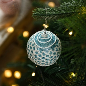 Close-up of blue glitter Christmas ball with white weave hanging on a festive tree