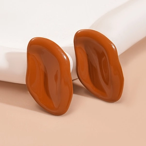 Close-up of glossy caramel resin irregular oval stud earrings on white wavy stand