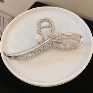 Detailed view of silver metal hair claw with elegant pearl embellishment on white plate