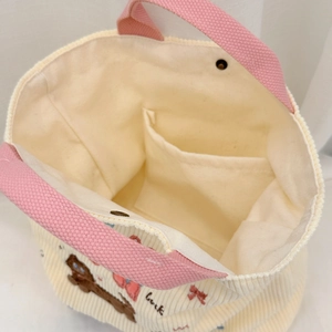Détail d'un sac en velours côtelé avec anses roses, bouton aimanté et broderie Luck