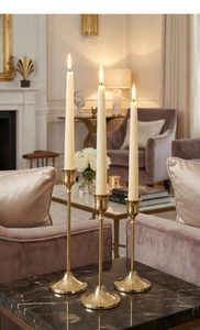Detalle de tres candelabros dorados elegantes con velas blancas sobre mesa de mármol