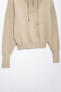 Detail of beige knit sweater featuring half-zip collar, drawstring, and ribbed texture