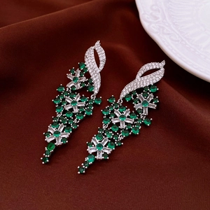 Close-up of elegant silver drop earrings with green zircons on dark velvet fabric