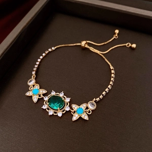 Detailed shot of an adjustable gold bracelet with green oval and blue side gemstones