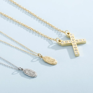 Flat lay of gold and silver religious portrait pendants with crystal X-shaped necklace