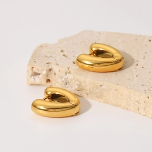 Close-up of polished 18K gold plated heart hoop earrings on textured stone