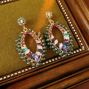 Détail de boucles d'oreilles bohèmes dorées avec zircons multicolores sur support velours
