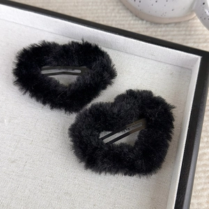Close-up of black plush heart-shaped hair clips on a beige fabric display tray