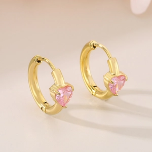 Detail of gold huggie earrings with a sparkling pink heart-shaped zircon stone