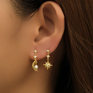 Close-up of asymmetrical gold celestial earrings with moon, star, pearls and zircons