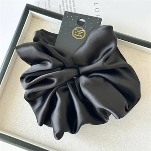 Detail of a large black satin scrunchie with silky texture and a handmade label
