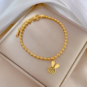 Dettaglio macro del bracciale a sfere dorate con ciondolo a coniglio e carattere Fu