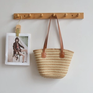 Detail of hand-woven straw tote with beige stripes and brown leather shoulder handles
