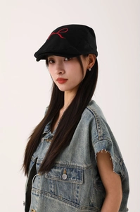 Détail d'une casquette gavroche noire avec un nœud rouge brodé sur le dessus