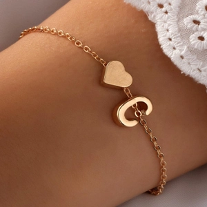 Détail d'un bracelet doré avec breloque cœur et lettre C porté sur de la dentelle