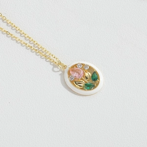 Close-up of gold chain necklace with floral pendant featuring pink and green zircon stones