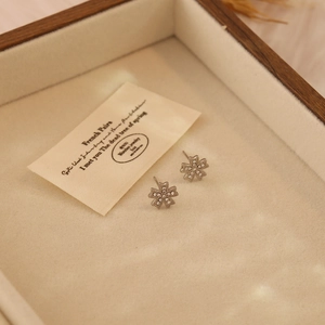 Macro detail of silver flower stud earrings with crystals in a wooden jewelry box