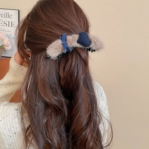 Detail view of a plush light brown hair claw with a dark blue bow and heart on a model