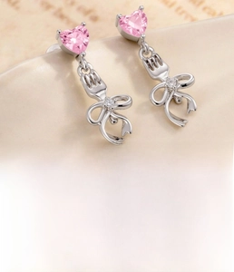 Macro detail of silver cartilage stud featuring pink heart zircon, bow, and fork charms