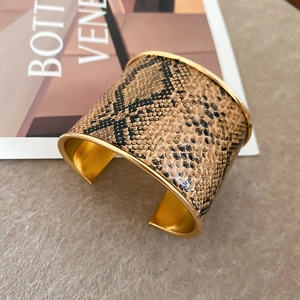 Detail of wide open gold cuff bracelet featuring brown snakeskin texture and metallic shine