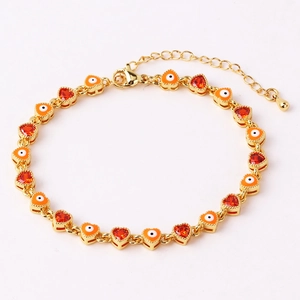 Detail van gouden hartbedeltjes met oranje oog en rode zirkoon op een hiphop armband