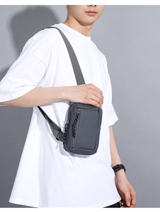 Detail of dark grey sports crossbody bag with vertical zipper and woven pull tab on chest