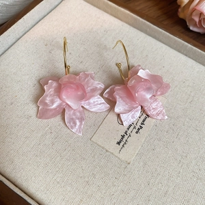 Détail de boucles d'oreilles fleurs en résine rose avec crochets dorés sur tissu