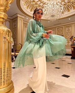 Detail of green chiffon flowy top paired with white wide-leg trousers in elegant setting
