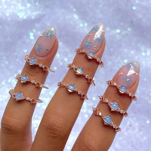 Close-up of rose gold Saturn rings with blue stones and crystals on manicured fingers