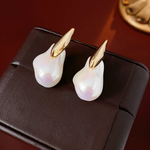Detail of gold-plated earrings with irregular pearls on brown leather jewelry box