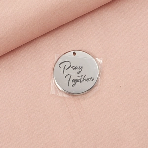 Macro shot of stainless steel round tag with Pray Together script on pink fabric