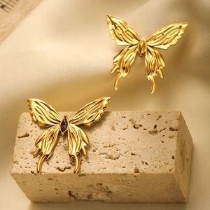 Detailed close-up of golden butterfly studs with purple gemstone on stone surface
