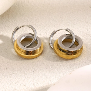 Detailed close-up of 18K gold and silver intertwined double star hoop earrings on beige background