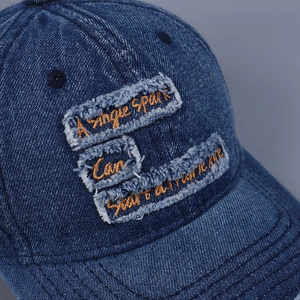 Detailed close-up of blue distressed denim baseball cap with embroidered orange letters