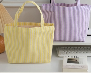 Detail of yellow and lilac striped canvas tote bags in a minimalist workspace setting