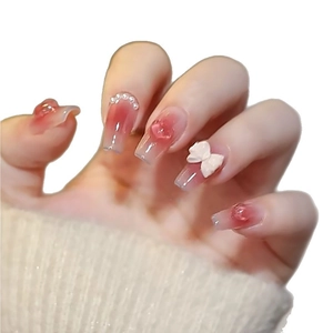Long pink ombre press-on nails with 3D bows, pearls, and heart charms on white background