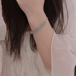 Detailed close-up of light green natural stone bead bracelet with silver metal charms