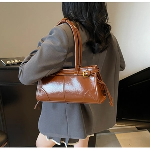 Close-up of a brown glossy leather shoulder bag with metallic buckle detail