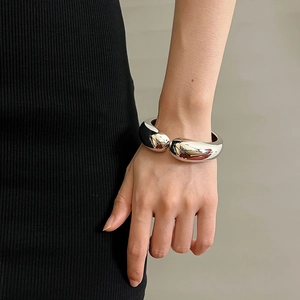 Detailed view of a wide polished silver metal cuff bracelet on a model's wrist