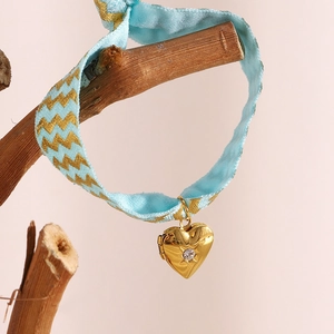 Close-up of heart locket with zircon on blue fabric strap wrapped on a wooden branch