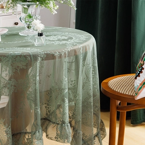 Pale green floral lace tablecloth with ruffled edges on a round wooden dining table