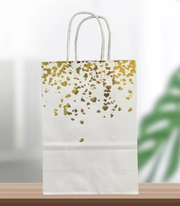 Detail of white paper gift bag with gold foil heart patterns and twisted paper handles